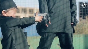 Screen shot from an ISIL video showing a militant giving a toddler a gun. Moments later in the video, the child shoots an 'apostate' to death.