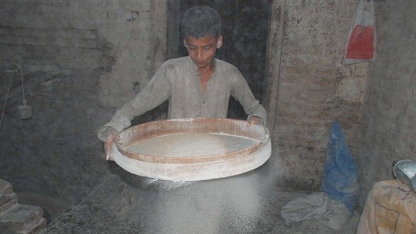 Ali's son Kashif helps his father sift flour. [Adeel Saeed]