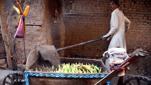 A worker in Peshawar puts hot sand in a hand cart full of fresh corn October 31. [Adeel Saeed]