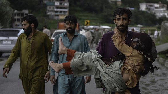 A man carries his sick daughter along a road damaged by floodwaters following heavy monsoon rains in the Madian area, Swat Valley, on August 27. [Abdul Majeed/AFP]