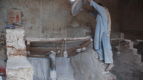 A worker pours wheat into the hopper for grinding by wheel-shaped stones moving in a circle. [Adeel Saeed]