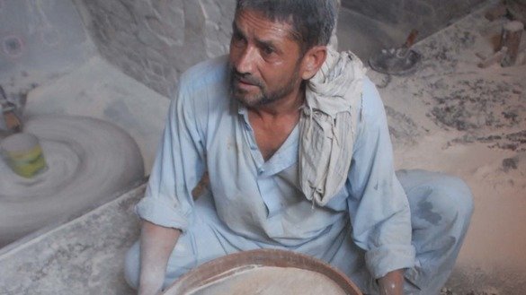 Hazrat Ali, operator of the water mill, sifts ground wheat to separate the bran and make the flour finer. [Adeel Saeed]