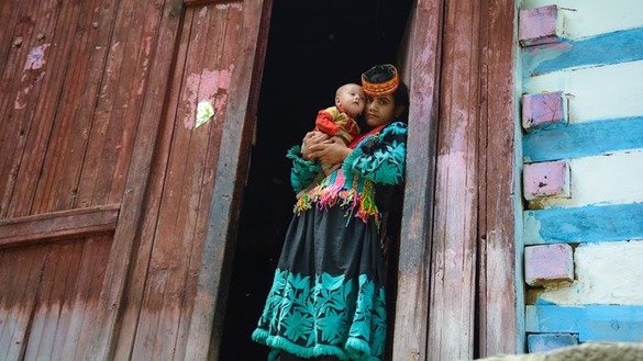 ایک کیلاش خاتون اپنے بچے کے ساتھ اپنے گھر کی دہلیز پر کھڑی ہے۔ [عالمگیر خان]