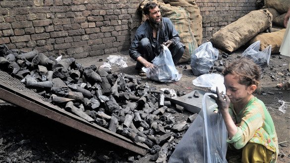 A girl packs a shopping bag with coal alongside her father in Peshawar ahead of Eid ul Adha on July 31. [Shahbaz Butt]