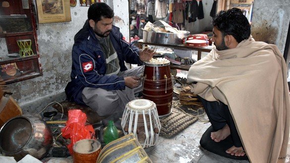 A visitor watches the repair of a hand drum in Peshawar on December 20. [Adeel Saeed]