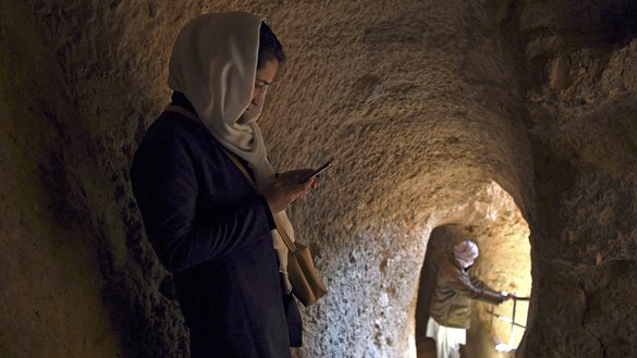 ایک ہزارہ خاتون، 3 مارچ کو بامیان کے بدھا کی جگہ پر راستے میں کھڑی اپنا فون دیکھ رہی ہے۔ ان بڑے بڑے مجسموں کے علاوہ اس جگہ پر قدیم غاروں، خانقاہوں اور مزاروں کا ایک سلسلہ بھی موجود ہے۔ [وکیل کوہسار/ اے ایف پی]