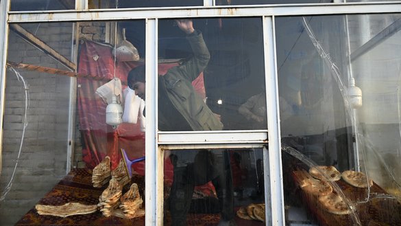 A baker cleans the window of a bakery as people wait to receive free bread distributed as part of the Save Afghans From Hunger campaign in Kabul on January 18. [Wakil Kohsar/AFP]