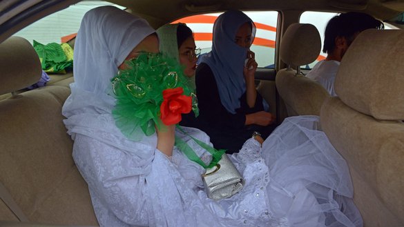 A bride (left) arrives in a car at the wedding hall for a mass marriage ceremony in Kabul on June 13. [Sahel Arman/AFP]
