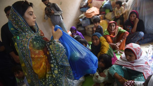 A woman distributes bags with relief items to displaced persons from flood-hit areas in Sindh province, in a school used as a temporary shelter in Karachi on August 27. [Rizwan Tabassum/AFP]