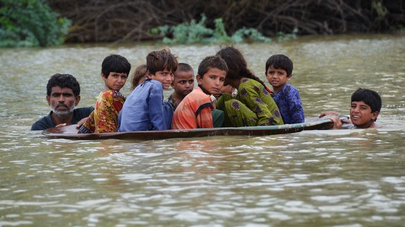 A man and a youth use a satellite dish to move children across a flooded area after heavy monsoon rainfalls in Jaffarabad district, Balochistan province, on August 26. [Fida Hussain/AFP]